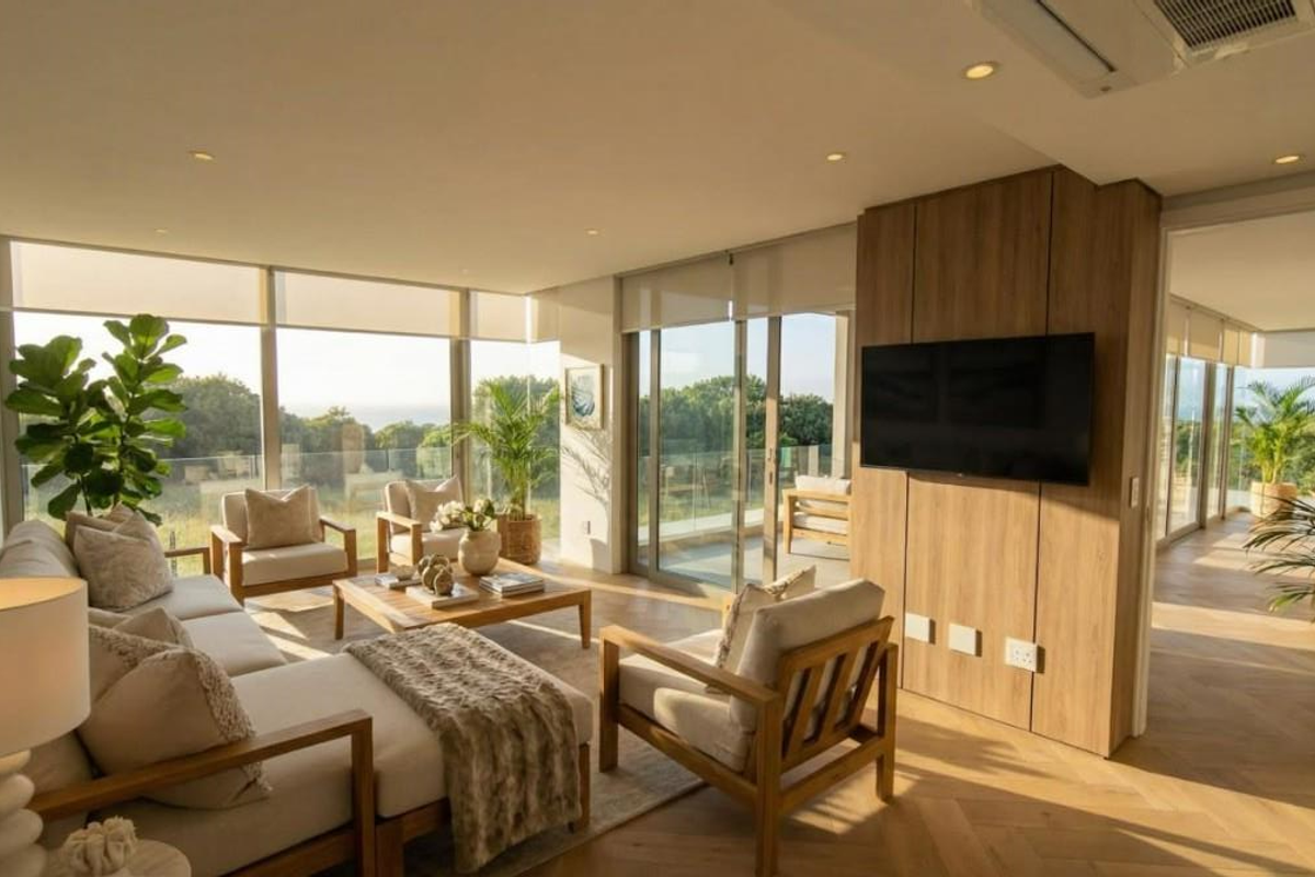 A bright, modern living room featuring herringbone timber flooring, floor-to-ceiling glass doors, and a timber-clad feature wall with integrated television.