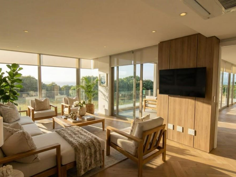 A bright, modern living room featuring herringbone timber flooring, floor-to-ceiling glass doors, and a timber-clad feature wall with integrated television.