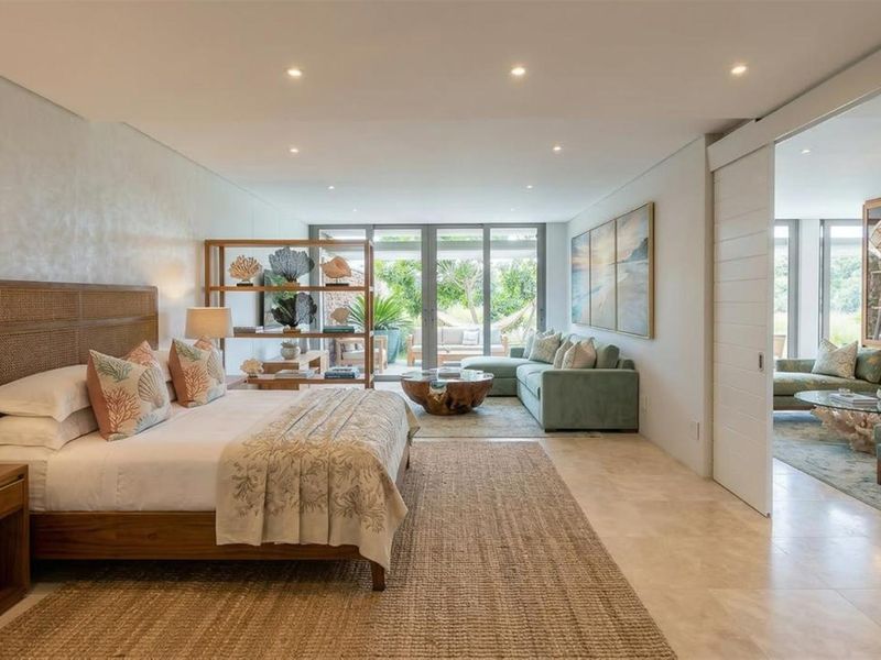 Spacious master bedroom suite featuring stone flooring, recessed lighting, and seamless access to an outdoor patio area through large glass sliding doors.