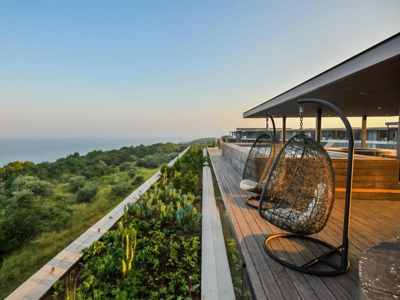 Spacious modern balcony featuring timber decking, a glass balustrade, and a raised garden bed with panoramic coastal and landscape views.