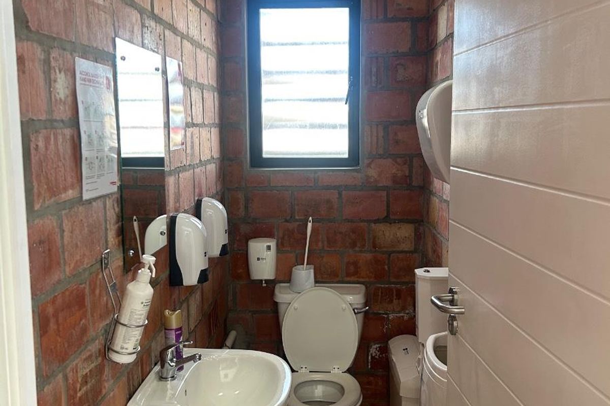 A functional commercial restroom featuring exposed brick walls, a wall-mounted basin, and a standard toilet suite with a window for natural ventilation.