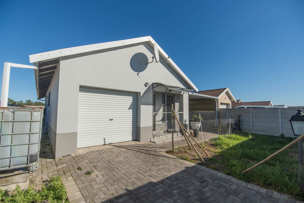 Exterior view of a residential property featuring a single garage, paved driveway, and a small garden area with perimeter walling.