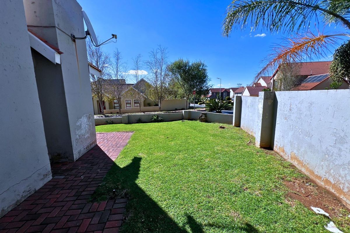 A rear garden area featuring a lawn, brick paved section, and boundary walls showing signs of weathered paint and surface staining.