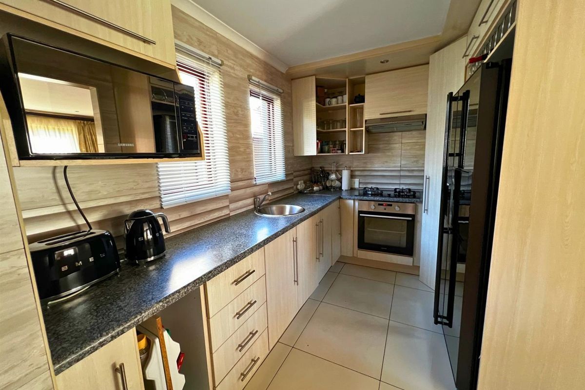 A functional kitchen featuring light wood-finish cabinetry, dark laminate countertops, built-in oven with gas hob, and tiled flooring.