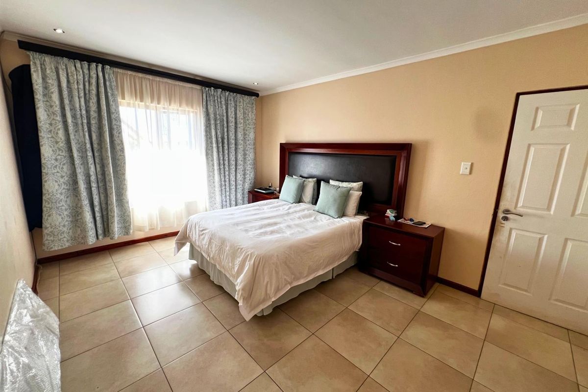 A spacious bedroom featuring neutral wall tones, large format floor tiles, and recessed ceiling lighting, providing a clean and functional living space.
