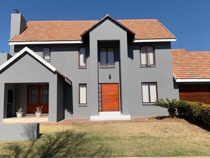 A well-maintained double-story residential house featuring a grey facade, tiled roof, timber entrance door, and integrated garage.