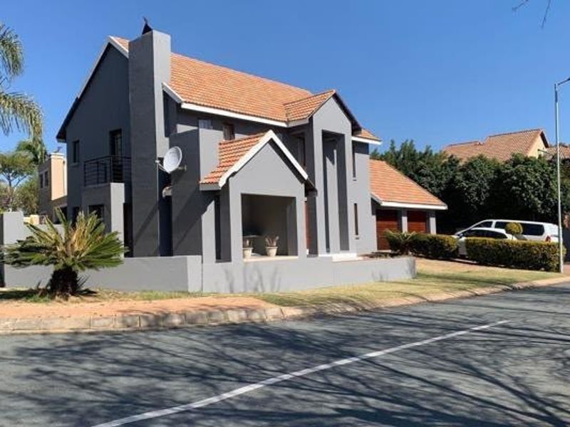 A well-maintained double-story residential house featuring a grey facade, tiled roof, chimney, and an integrated double garage with a paved driveway.
