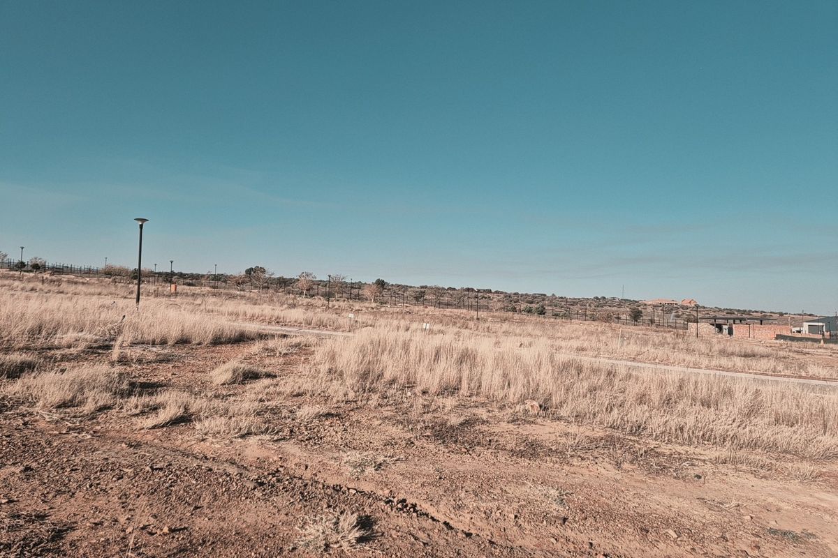 A view of a vacant residential plot featuring natural grass, perimeter fencing, and street lighting infrastructure.