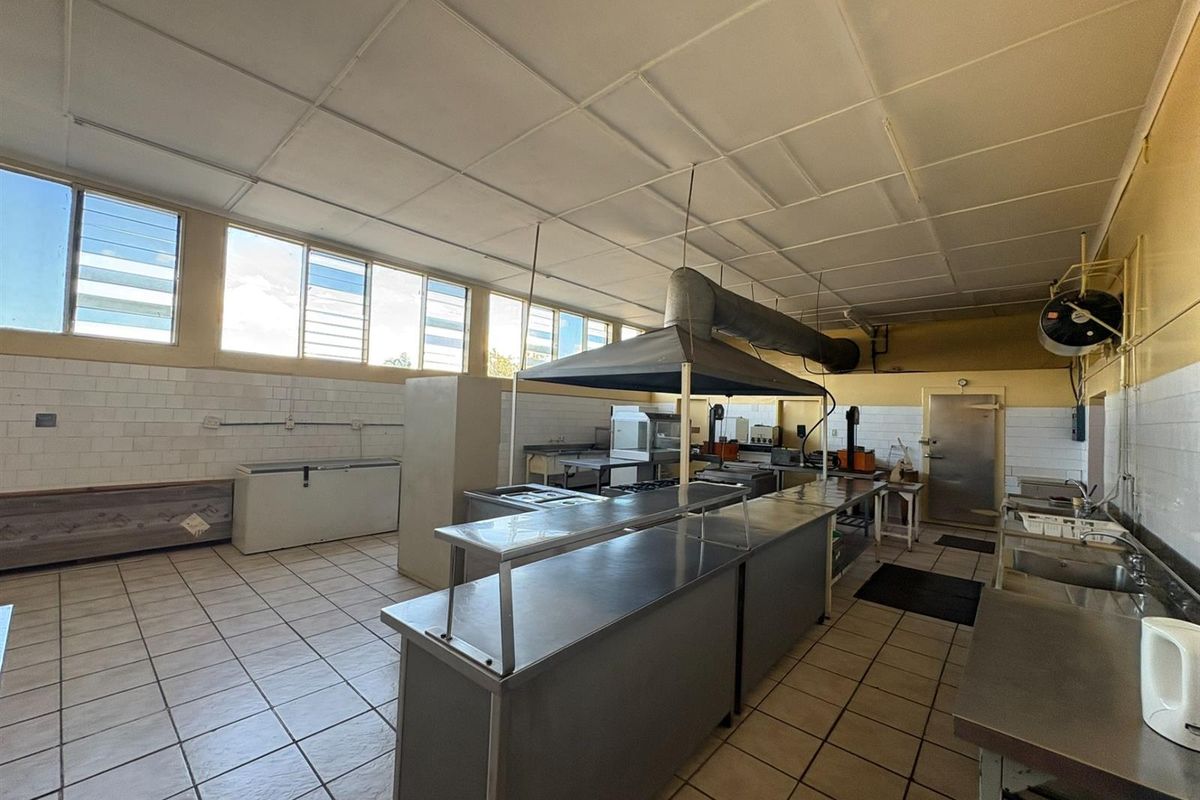 A spacious commercial kitchen featuring stainless steel work surfaces, an industrial extractor hood, tiled flooring, and wall splashbacks, suitable for high-volume food preparation.