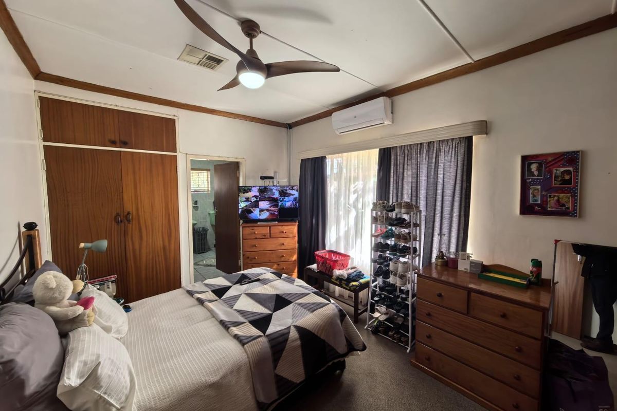 A functional bedroom featuring built-in wooden wardrobes, a ceiling fan, and a wall-mounted air conditioning unit.
