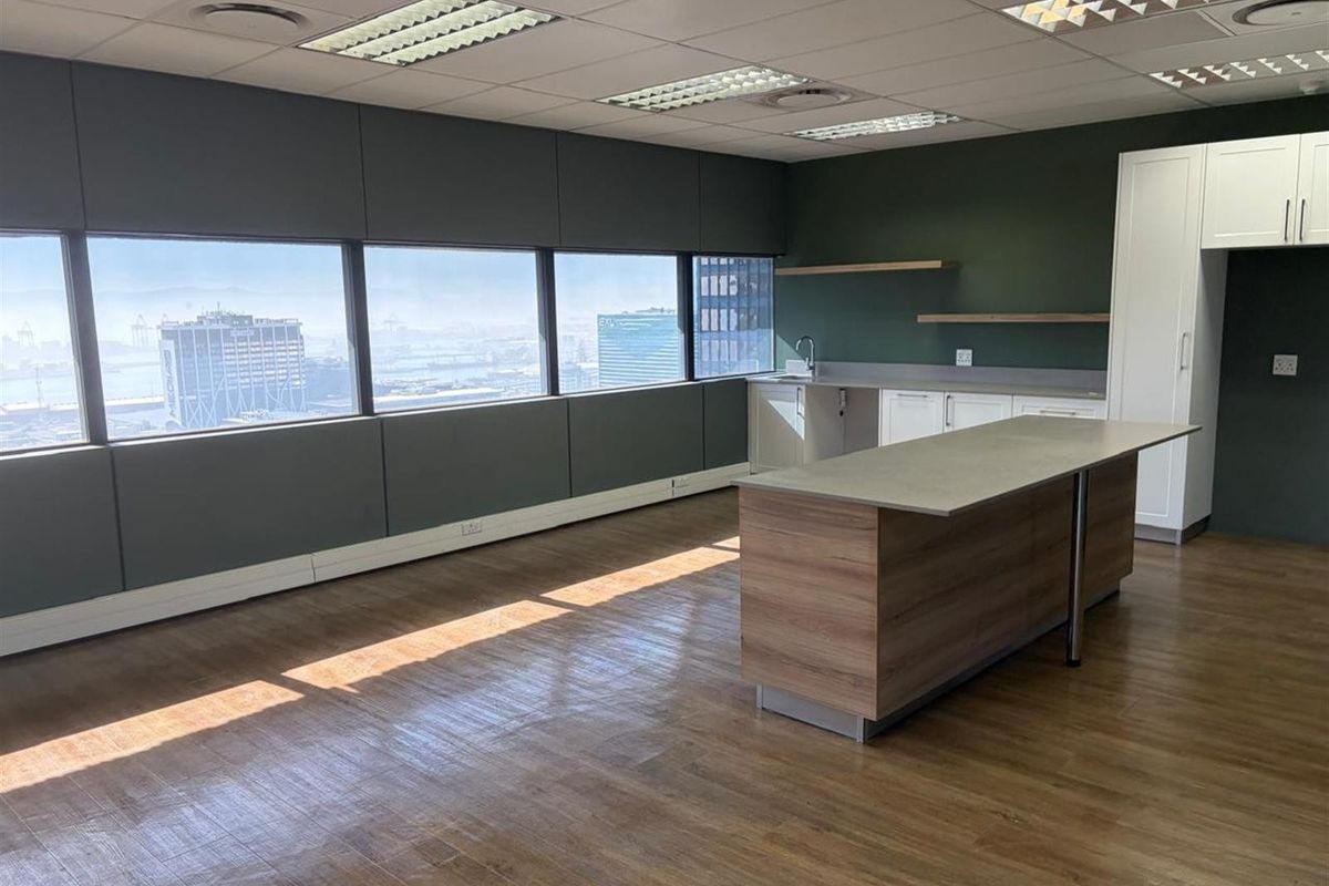 Modern office kitchenette featuring a central island, built-in cabinetry, floating shelves, and large windows offering expansive city views.