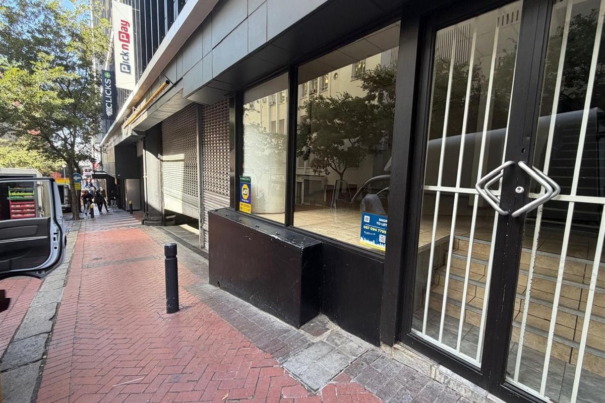 Street-level retail storefront featuring large display windows, secure metal entrance gate, and direct access to a paved pedestrian walkway.