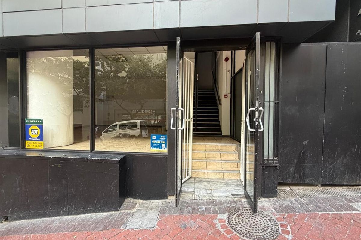 Street-level retail entrance featuring large display windows, metal security gates, and internal staircase access to the upper level.