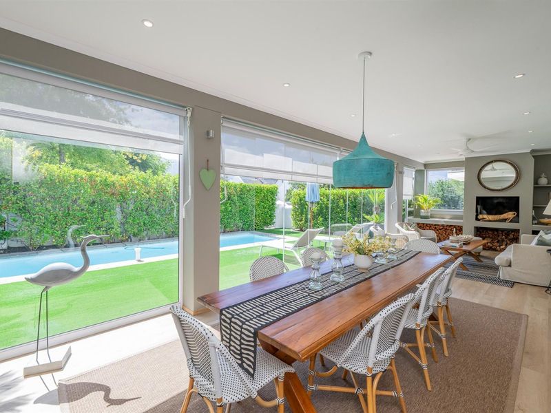 Spacious open-plan living and dining area featuring large sliding glass doors, recessed lighting, and a built-in fireplace, overlooking the pool and garden.