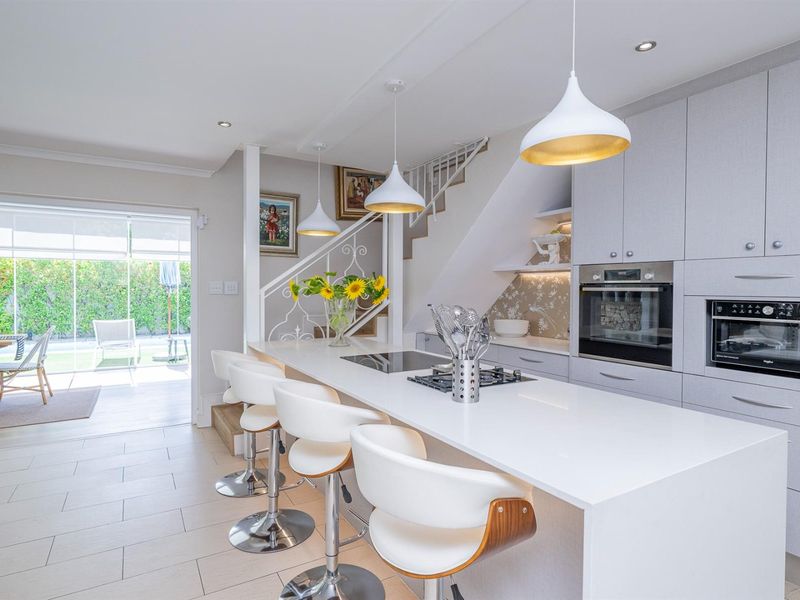 Modern open-plan kitchen featuring a central island with integrated hob, built-in appliances, and sleek cabinetry, seamlessly flowing into the adjacent outdoor patio area.