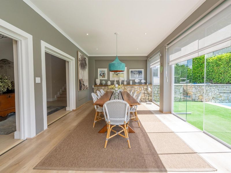 Bright dining room featuring hardwood floors, a stone accent wall, and large sliding glass doors providing seamless access to the garden and pool area.