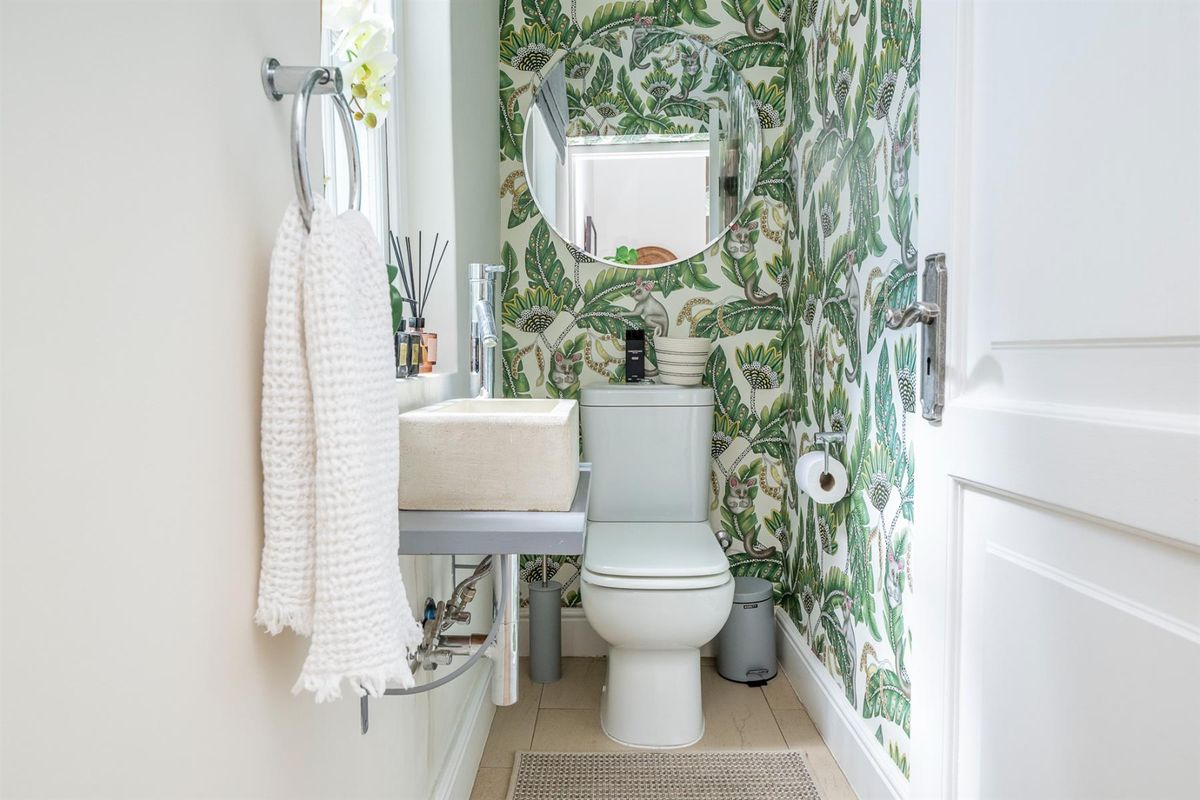 A compact powder room featuring a wall-mounted stone basin, chrome fixtures, and bold botanical wallpaper.