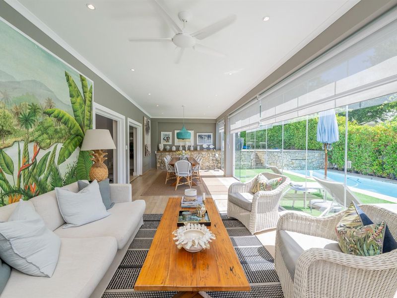 Bright open-plan living and dining area featuring timber flooring, recessed lighting, and large glass doors opening to the pool area.