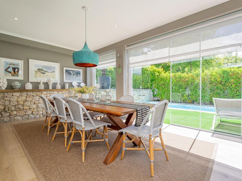 Bright dining room featuring a stone accent wall, timber flooring, and large sliding glass doors providing seamless access to the pool and garden area.