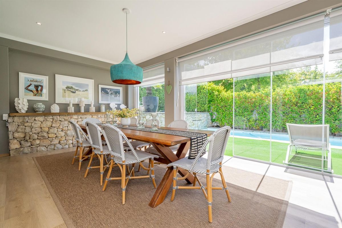 Bright dining room featuring a stone accent wall, timber flooring, and large sliding glass doors providing seamless access to the pool and garden area.