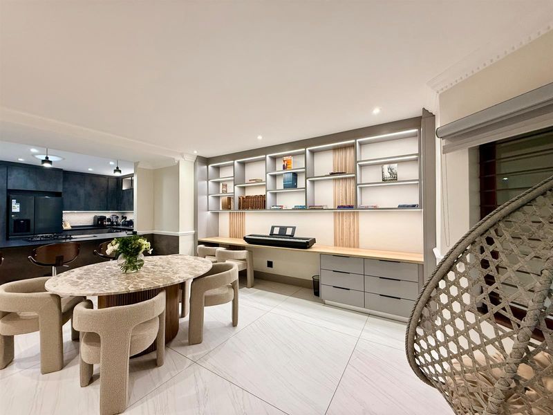 Modern open-plan living area featuring a sleek kitchen with dark cabinetry and a custom built-in study or display wall with integrated lighting.