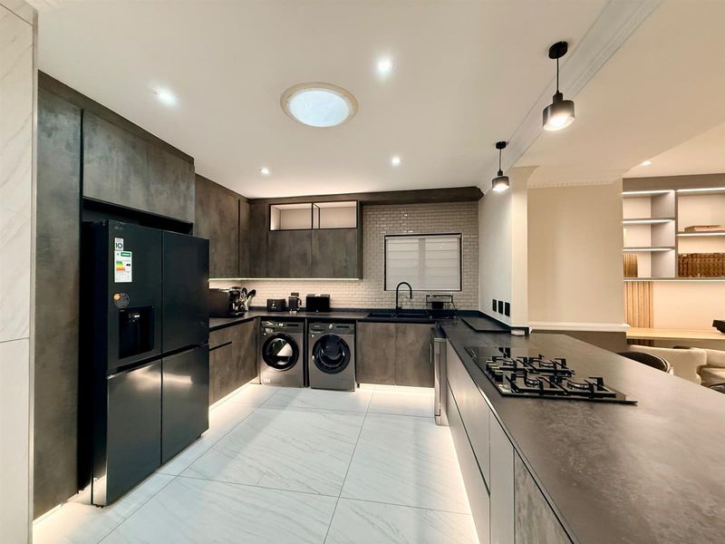 Modern, high-end kitchen featuring dark cabinetry, stone countertops, integrated appliances, gas hob, subway tile backsplash, and excellent recessed lighting with a skylight.
