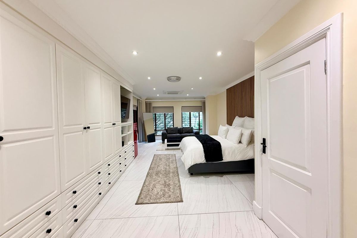 Spacious bedroom featuring extensive built-in cabinetry, modern tiled flooring, recessed lighting, and a decorative slatted wood feature wall behind the bed area.