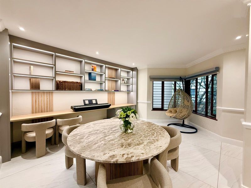 A well-lit living area featuring custom built-in shelving with integrated lighting, large windows with security bars, and modern tiled flooring.