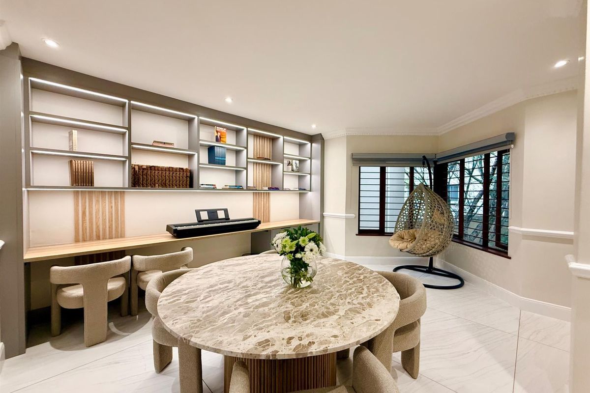 A well-lit living area featuring custom built-in shelving with integrated lighting, large windows with security bars, and modern tiled flooring.