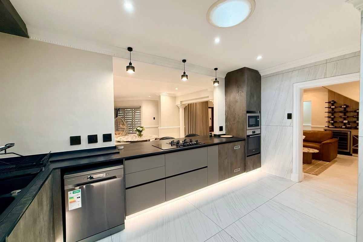 Modern kitchen featuring sleek cabinetry, stone countertops, integrated appliances, gas hob, and marble-look flooring with ambient under-cabinet lighting.