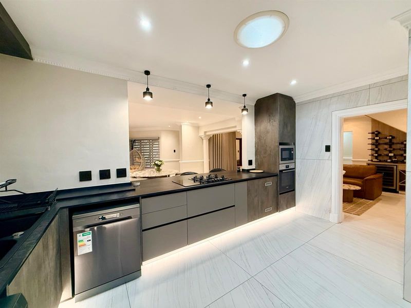 Modern kitchen featuring sleek cabinetry, stone countertops, integrated appliances, gas hob, and marble-look flooring with ambient under-cabinet lighting.