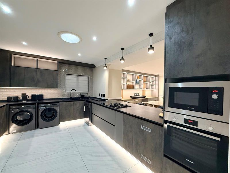 Modern, high-end kitchen featuring dark integrated cabinetry, stone countertops, built-in Bosch appliances, subway tile backsplash, and elegant recessed lighting with a skylight.