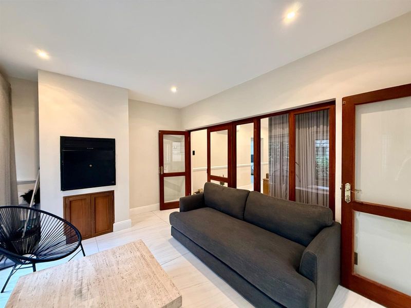 A bright living room featuring tiled flooring, a built-in fireplace with wooden cabinetry, and timber-framed glass doors providing access to adjacent spaces.