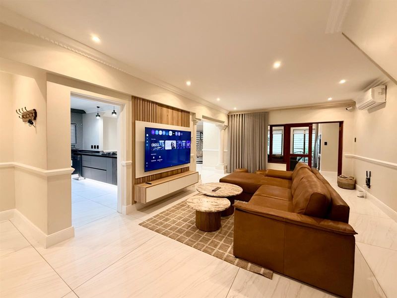 A modern, well-maintained living room featuring elegant wainscoting, crown molding, tiled floors, and a stylish timber slat feature wall with a built-in media console.