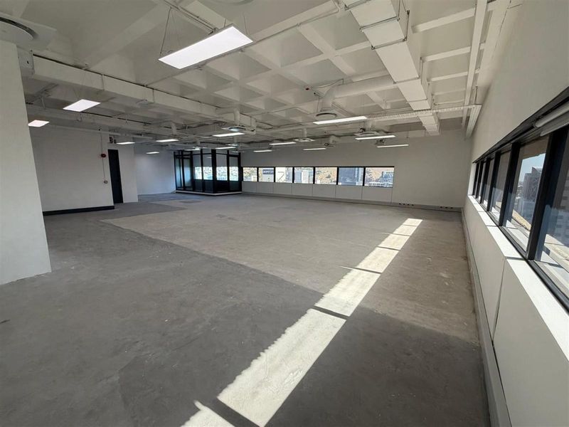 Spacious open-plan office area featuring exposed industrial-style ceilings, large windows providing natural light, and polished concrete flooring.
