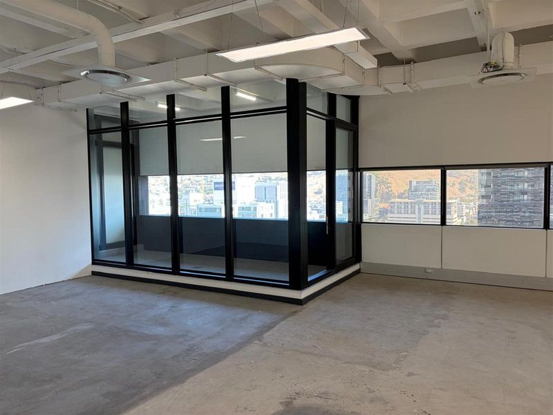 Open-plan office space featuring exposed ceiling beams, black-framed glass partitioning, and large windows with city views.