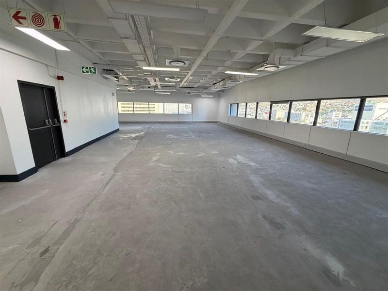 A spacious, open-plan office area featuring an exposed ceiling, large windows with city views, and unfinished concrete flooring, ready for custom fit-out.