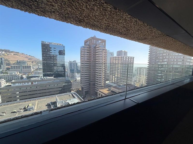 A clear, elevated city skyline view captured from a balcony with a modern glass balustrade and textured architectural detailing.