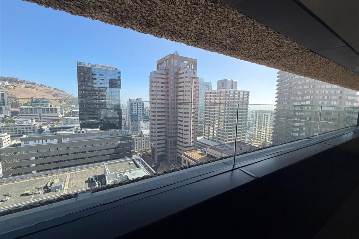 A clear, elevated city skyline view captured from a balcony with a modern glass balustrade and textured architectural detailing.