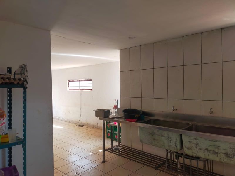 A functional scullery or utility prep area featuring a stainless steel double sink, tiled splashback, and ceramic floor tiles.