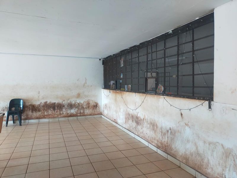 An empty office space featuring tiled flooring and a security grille, currently requiring significant wall repairs and cosmetic refurbishment.