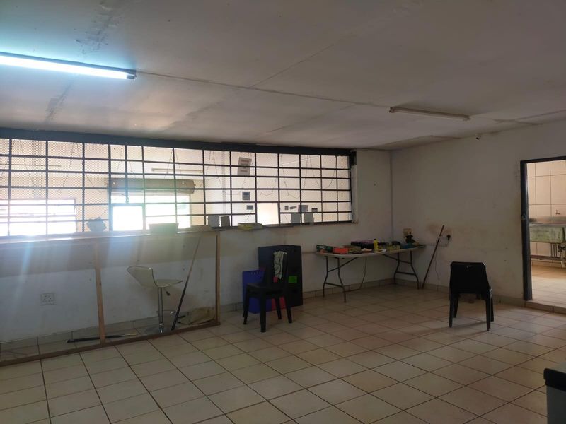 An open-plan commercial space featuring tiled flooring, fluorescent lighting, and security bars on the windows, presenting a blank canvas for renovation.