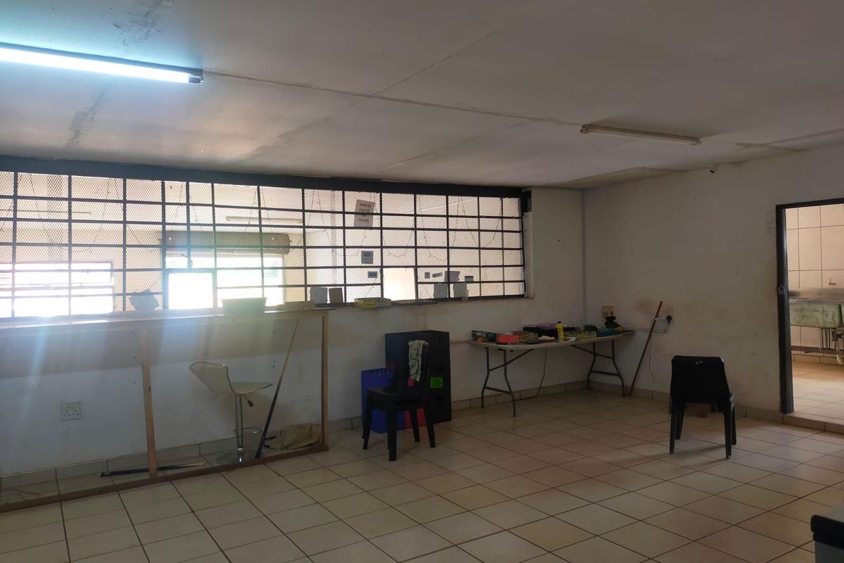 An open-plan commercial space featuring tiled flooring, fluorescent lighting, and security bars on the windows, presenting a blank canvas for renovation.