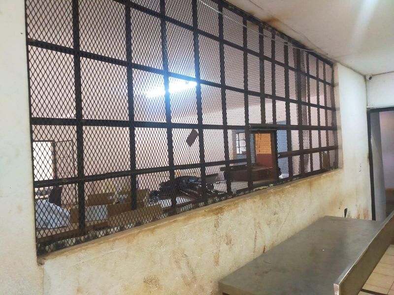 Utility space featuring a large security grille partition and a fixed metal counter, showing significant signs of wear and wall staining.