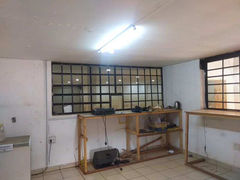 A functional utility or workspace area featuring tiled floors, security bars on windows, and basic electrical infrastructure, requiring cosmetic updates.