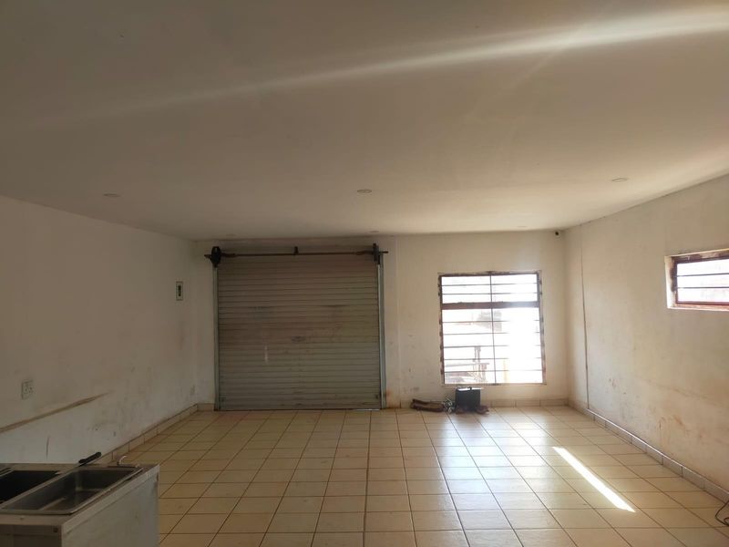An empty, functional garage space featuring tiled flooring, a roller shutter door, security bars on windows, and a built-in stainless steel sink.