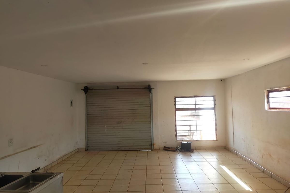 An empty, functional garage space featuring tiled flooring, a roller shutter door, security bars on windows, and a built-in stainless steel sink.