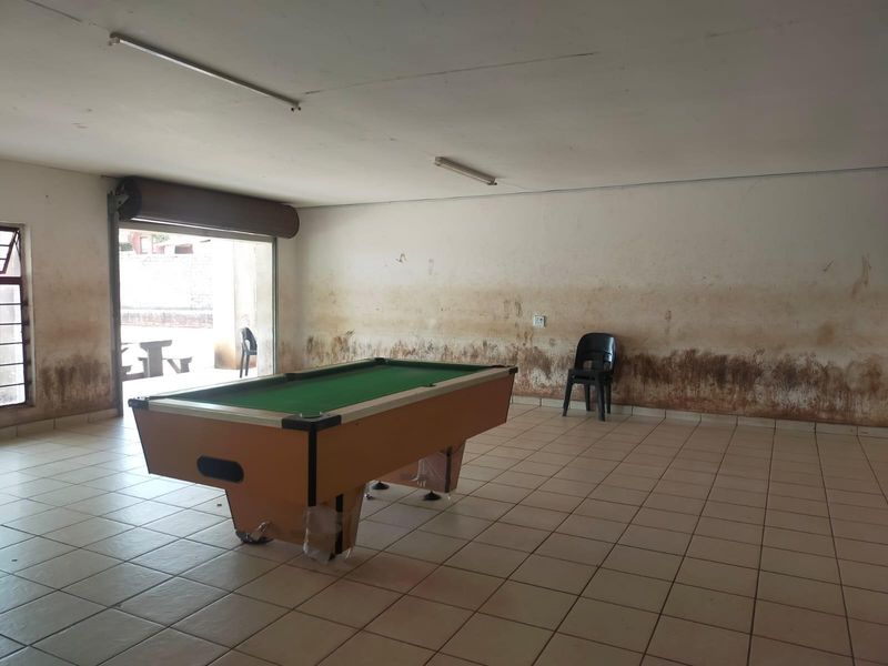 A spacious interior area featuring tiled flooring and a roller shutter door, currently showing significant wall damage and staining requiring maintenance.