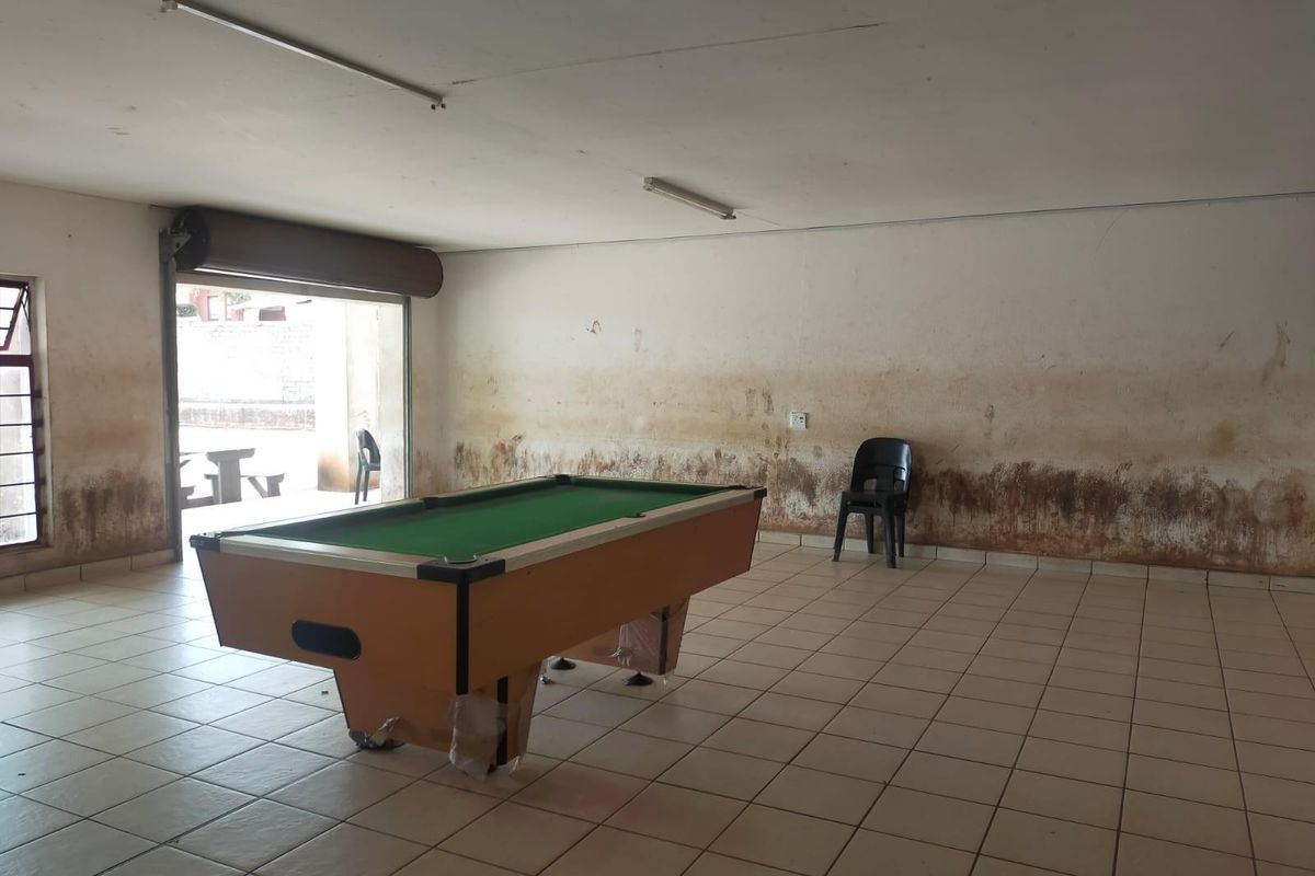 A spacious interior area featuring tiled flooring and a roller shutter door, currently showing significant wall damage and staining requiring maintenance.