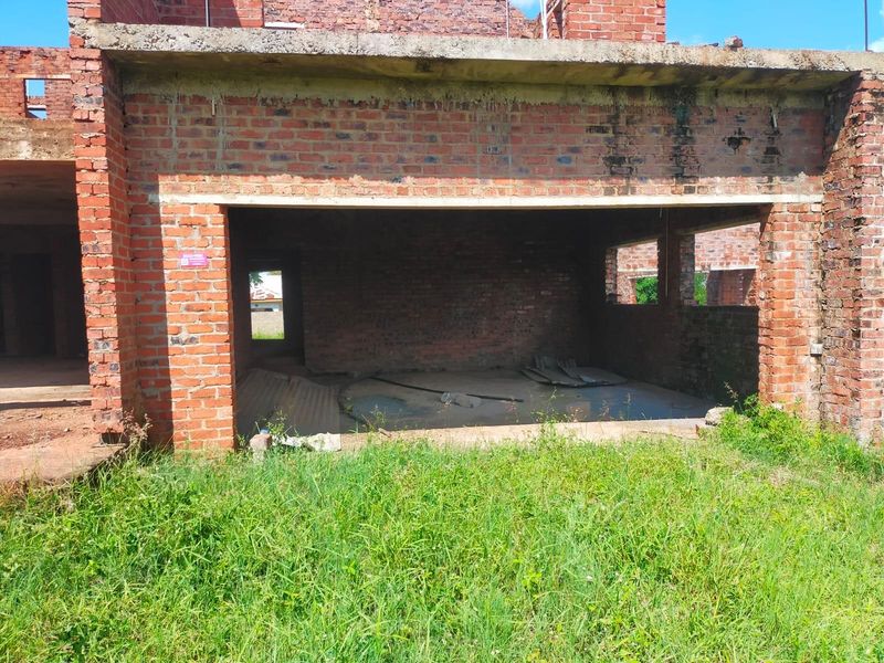 An unfinished residential structure showing exposed brickwork and concrete slab, currently in a shell state requiring significant completion and finishing work.